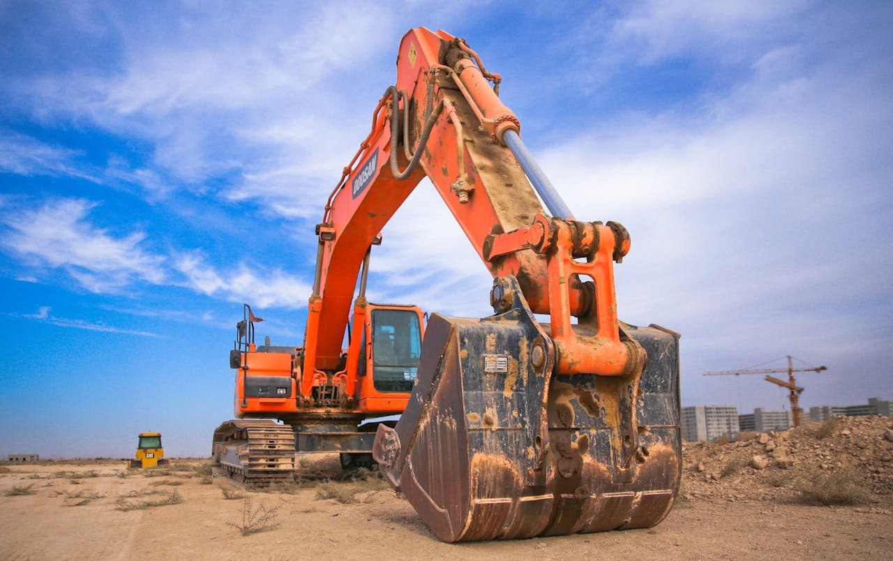 Services-03 A large orange excavator working on a construction site under a blue sky.