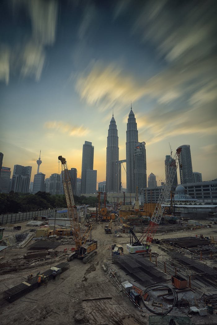 creative Dramatic view of the Petronas Towers towering over a busy construction site in Kuala Lumpur at sunset.